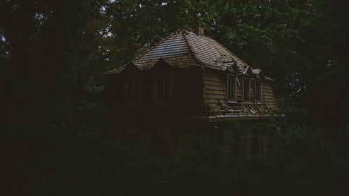 Abandoned house amidst trees on field against sky