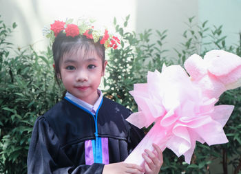 Portrait of innocent girl holding prop while standing against plants