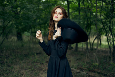 Portrait of young woman standing against trees