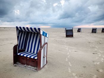 Hooded beach chairs on sand against cloudy sky