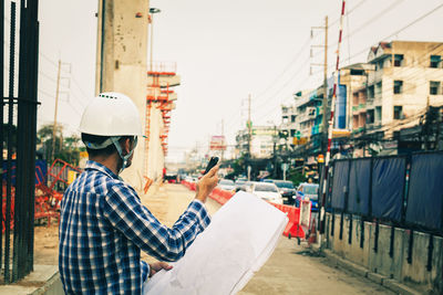 Rear view of man holding mobile phone on street