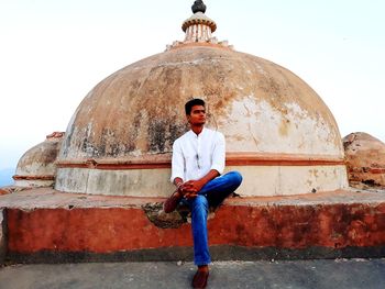 Portrait of young man sitting against built structure