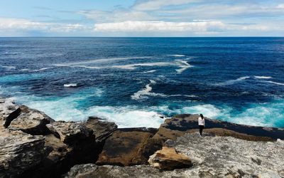 Rear view of woman looking at sea while standing on rock