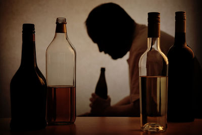 Sad man holding alcohol bottle by table at home