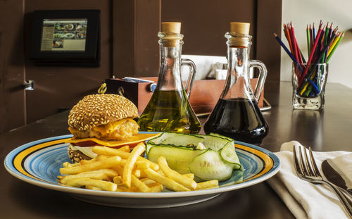 Close-up of hamburger with french fries and cucumber served in plate on table