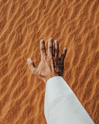Cropped hand of man gesturing against sand in desert