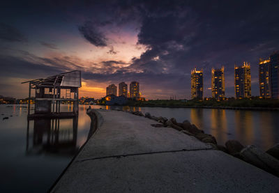 Pier over river against sky at sunset