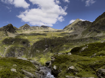 Scenic  view of mountain peaks, clouds and a mountain stream against sky.