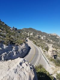 Road leading towards mountains against clear blue sky