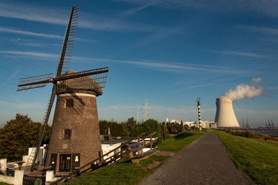 Windmill by factory against sky