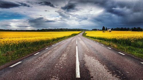 Road passing through field against cloudy sky