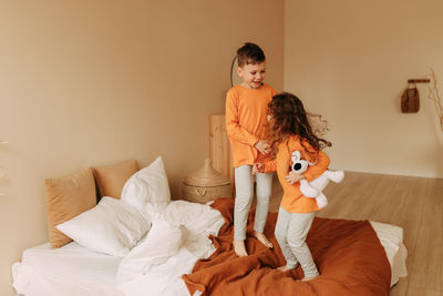Funny happy kids brother and sister in pajamas playing having fun in a cozy bedroom at home