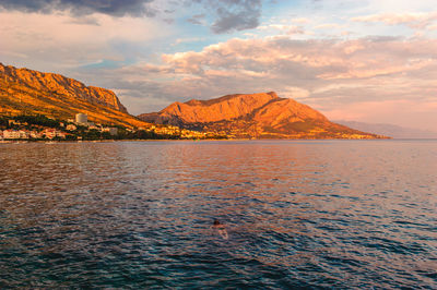 Scenic view of sea by mountains against sky during sunset