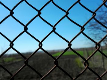 Field seen through chainlink fence against clear blue sky