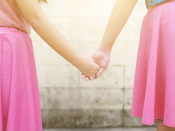 Midsection of sisters holding hands while standing against wall