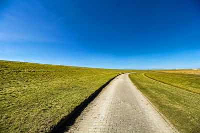 Road amidst field against blue sky