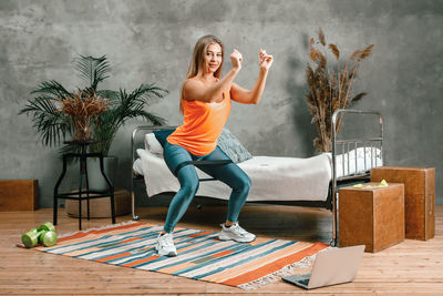 Cheerful sporty woman with blond hair doing a squat with sport fitness rubber bands 
