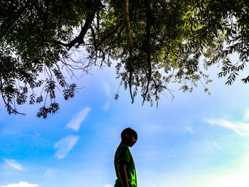 Low angle view of boy standing by tree against sky