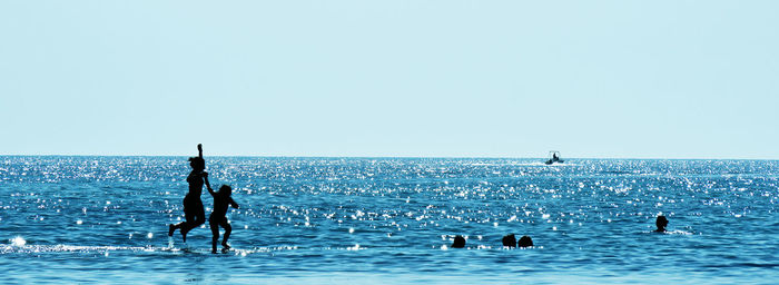 Silhouette people enjoying in calm sea against clear sky