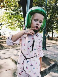 Cute girl wearing crash helmet while standing on sidewalk against trees