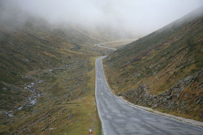 Road passing through mountains during foggy weather