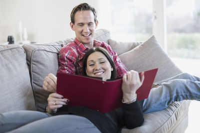 Happy couple looking at photo album together on sofa
