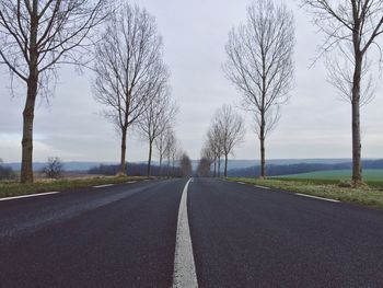 Empty road amidst trees against sky