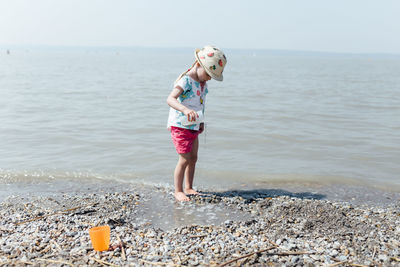 Full length of girl pouring water while standing on shore at beach