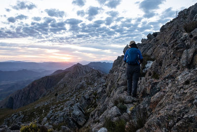 Woman with blue backpack hiking on mountain slope during sunrise 