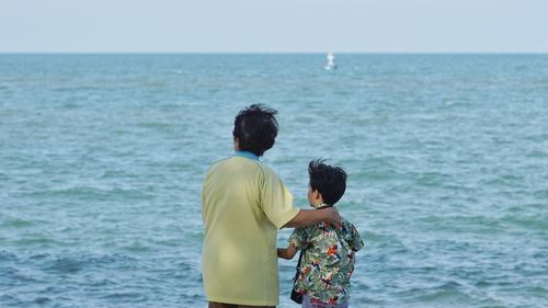 Rear view of grandmother and grandson standing at beach against sky