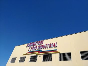 Low angle view of text on building against clear blue sky