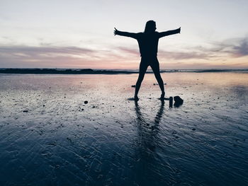 Silhouette woman standing with arms outstretched at beach during sunset