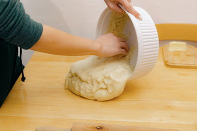 The hand of a caucasian young girl pours dough from a bowl onto the table.