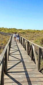 People walking on footbridge against clear blue sky