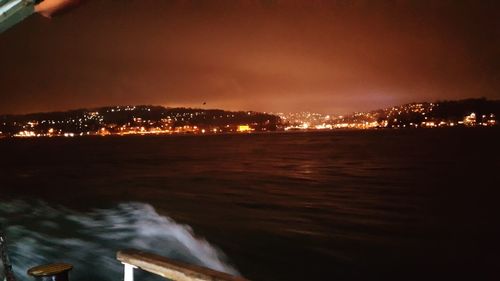 Illuminated city by sea against sky at night