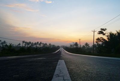 Road by trees against sky during sunset