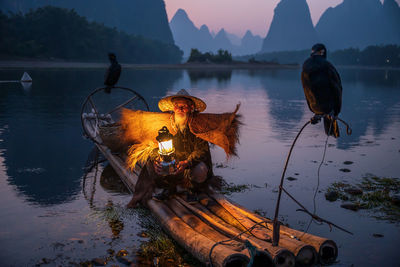 Portrait of man wearing hat crouching on raft against mountain and sky