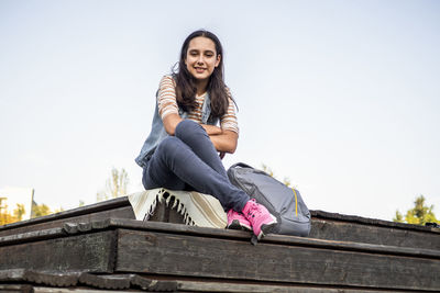 Low angle view of young woman sitting on roof against sky