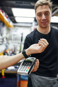 Soft focus of male mechanic with terminal receiving contactless payment from crop customer with smart watch during work in garage