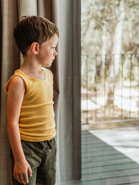 Serene little child standing near window in cottage and looking away in thoughts