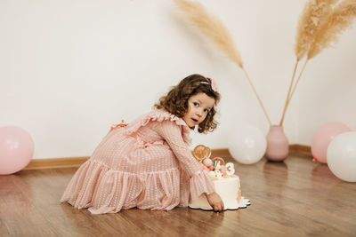 A cute little girl is sitting on the floor next to a cake for her birthday. holiday, birthday, cake