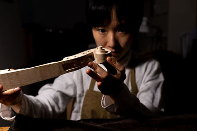 Young chinese female violin maker working on the neck of violin under construction in her workshop