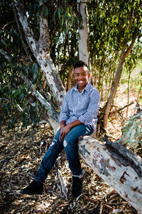 Full length of young man sitting on tree trunk in forest