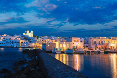 Illuminated buildings by sea against sky at dusk