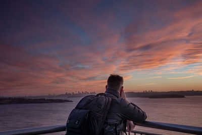 Rear view of man looking at sea against sky during sunset