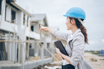 Side view of young woman holding smart phone while standing against buildings