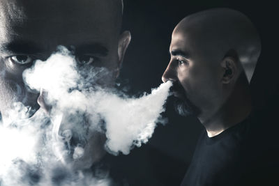 Close-up of young man smoking against black background