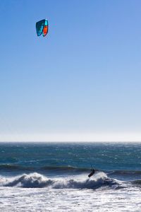 Person paragliding over sea against clear blue sky