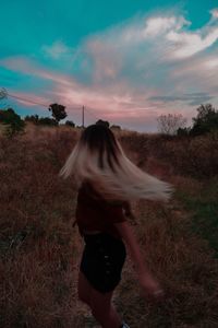 Rear view of woman walking on field against sky