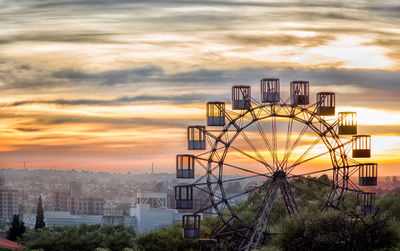 Ferris wheel in city against sky at sunset